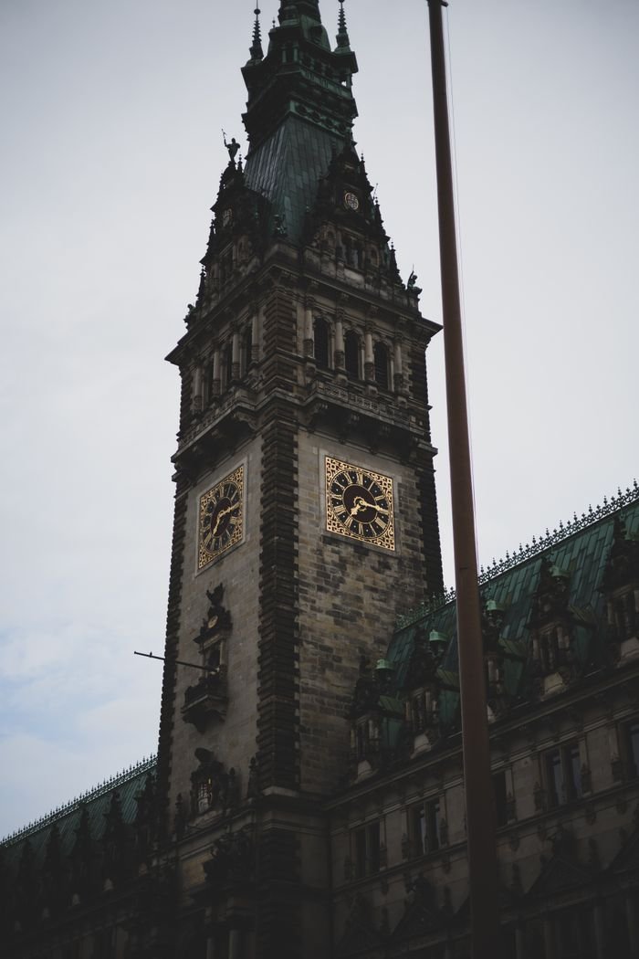 Dramatic view of the Gothic clock tower at Hamburg City Hall, Germany, under a cloudy sky.