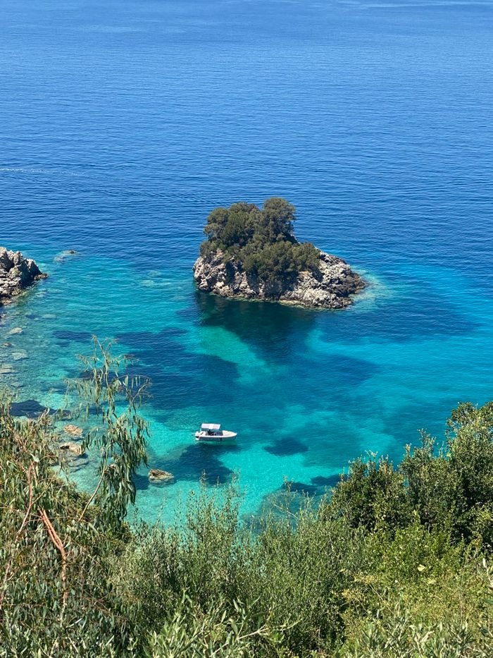 A small boat floats near a lush island in crystal-clear waters, offering a serene Greek seascape.